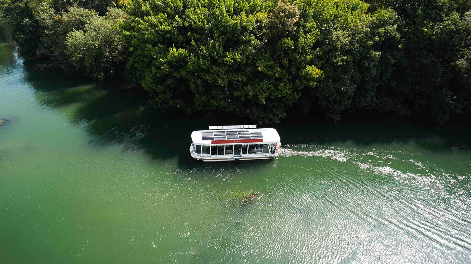 Hennessy solar-powered boat cruising along the Charente River in Cognac, amidst pristine greenery
