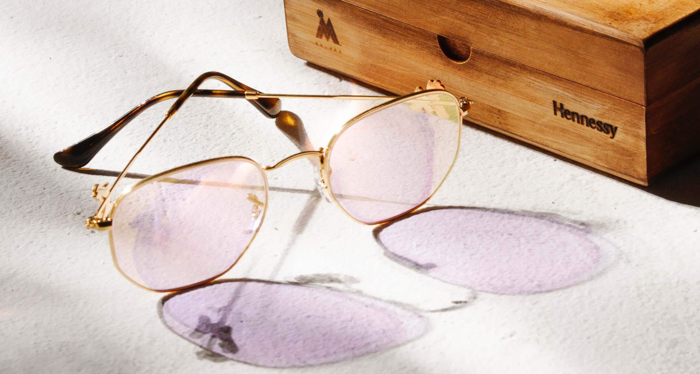 A pair of modern sunglasses with rose-tinted lenses, 14 karat gold plating, and 14 karat gold medallions.