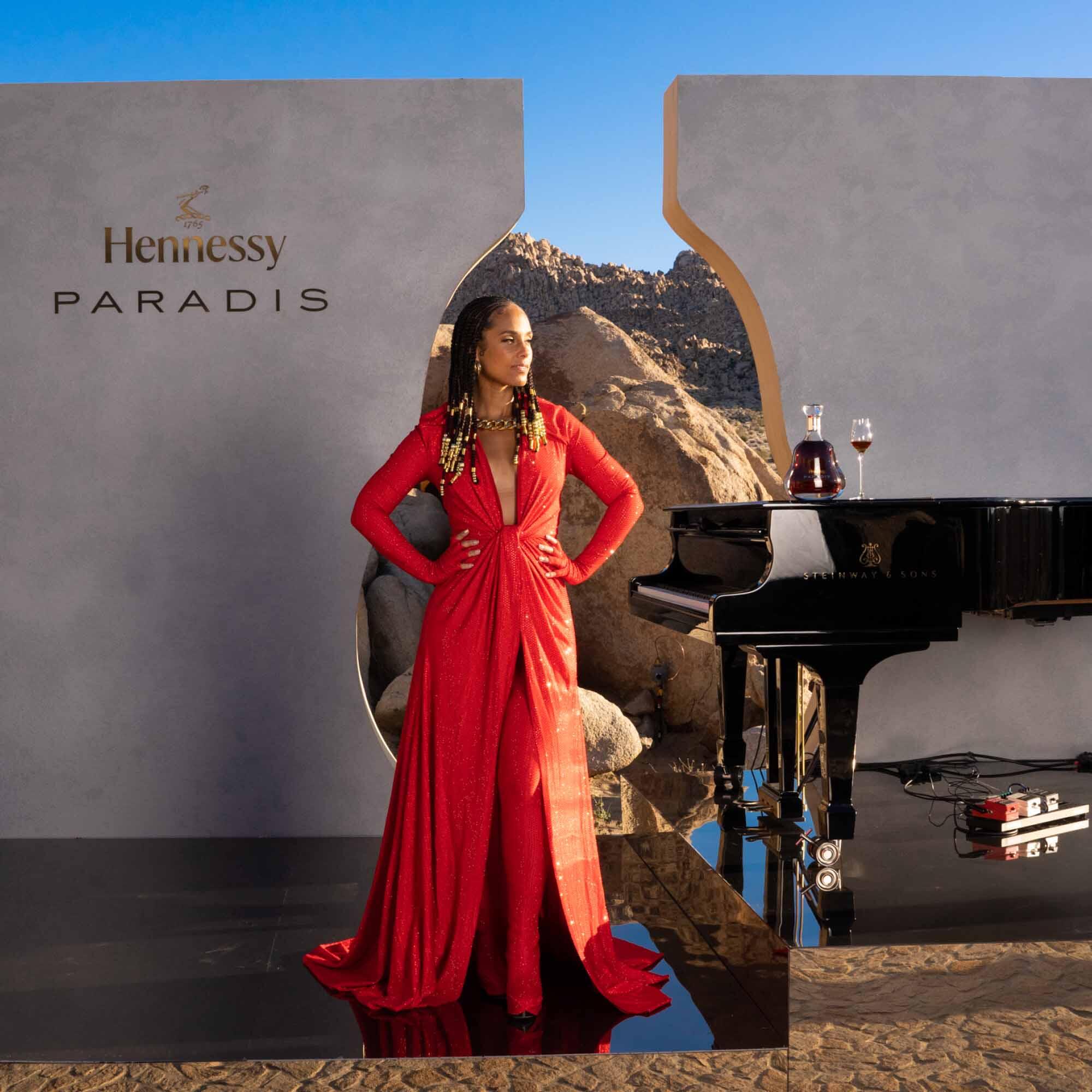Alicia Keys standing triumphantly while a grand piano and a bottle of Hennessy Paradis complement her grace.