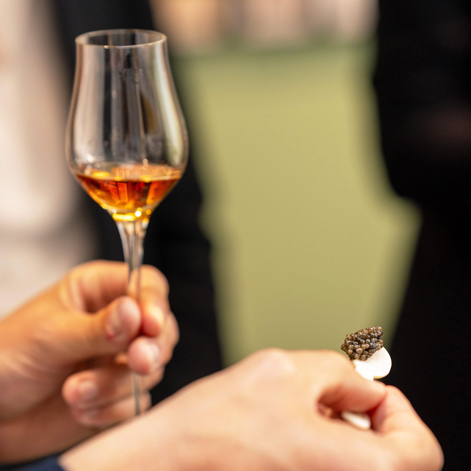 A guest is holding a glass of Hennessy Paradis in his left hand, and a mother-of-pearl spoon with caviar in his right hand