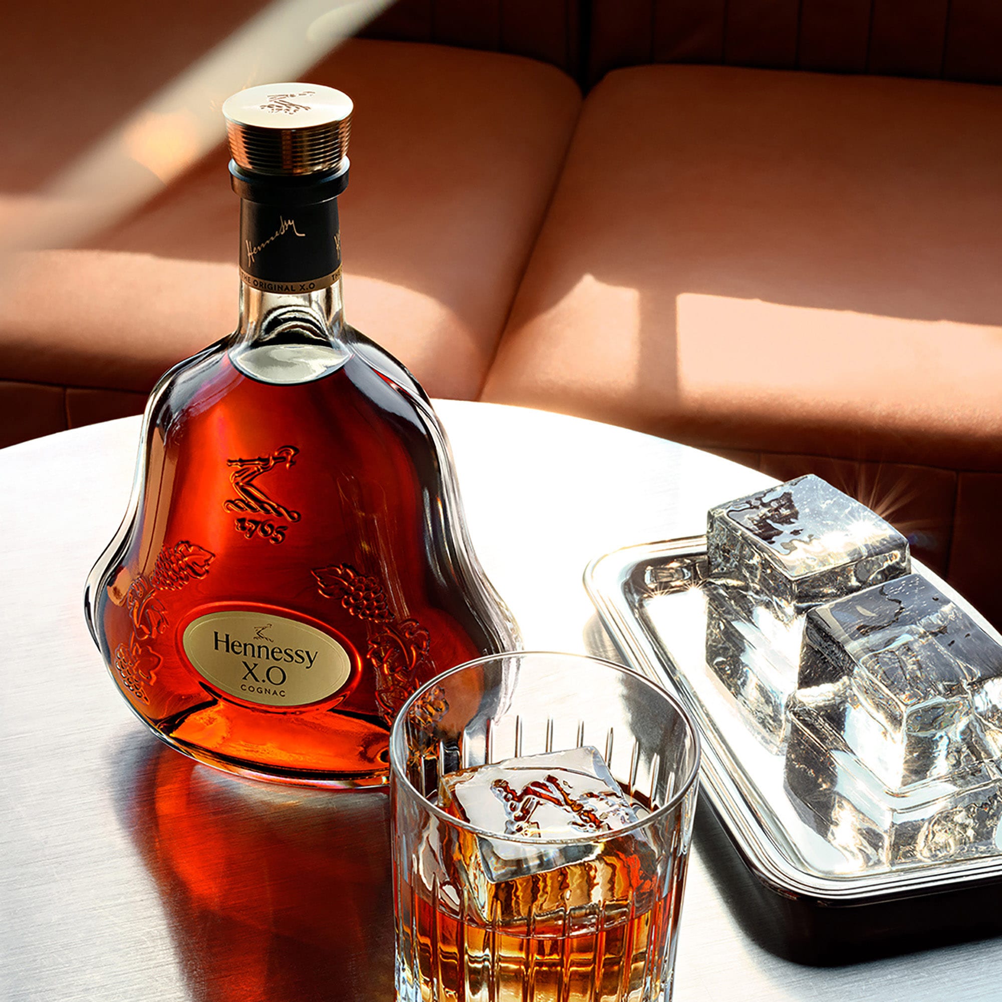 Decanter of Hennessy X.O on a coffee table, next to a glass of cognac and large ice cubes